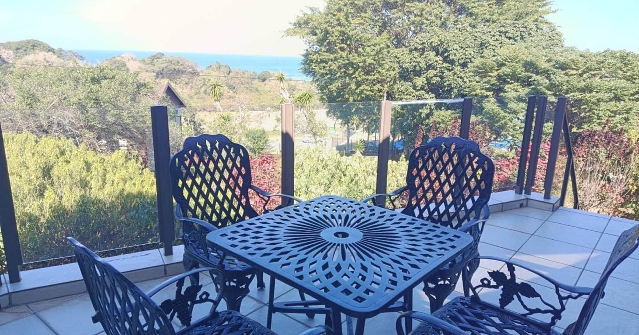 An outdoor patio with a table and chairs, overlooking a scenic landscape with trees and a view of the ocean.