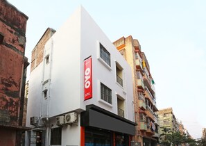 Un edificio moderno con un llamativo letrero rojo y blanco, unidades de aire acondicionado y un balcón visible.