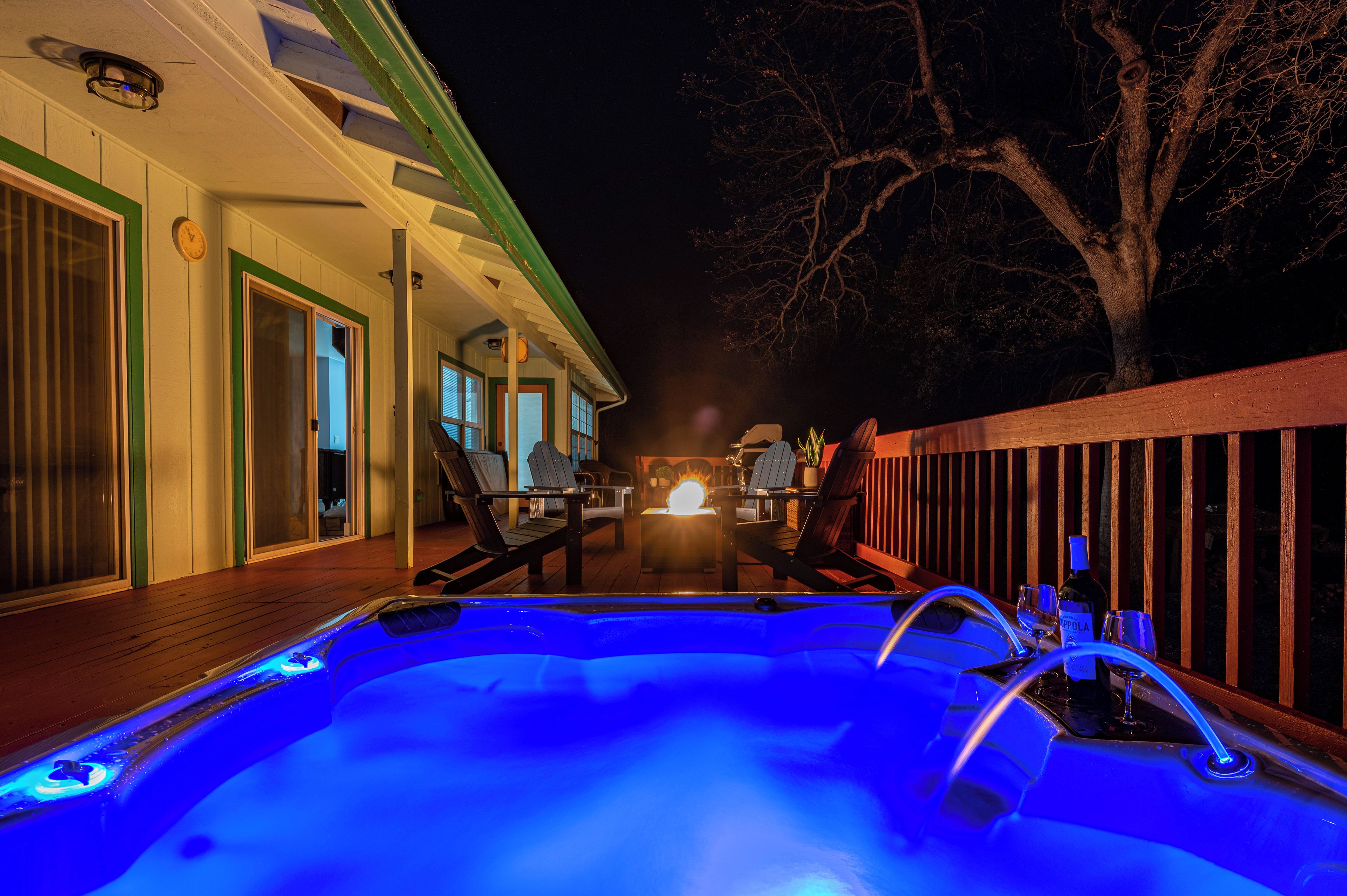 A hot tub with blue lighting, outdoor seating, and a view of a house with a porch.