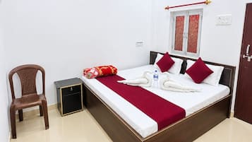 A hotel room with a bed, a chair, an air conditioning unit, a window with a curtain, and a red patterned rug.