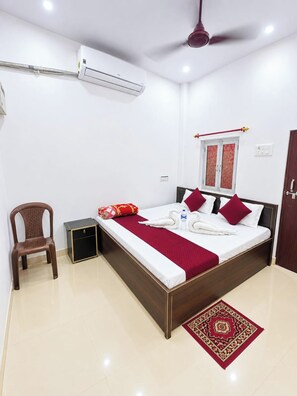 A hotel room with a bed, a chair, an air conditioning unit, a ceiling fan, and a window with curtains.