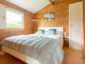 A wooden-paneled bedroom with a bed, pillows, a painting, and a window. - Holiday Home in Renesse With Swimming Pool (Renesse)