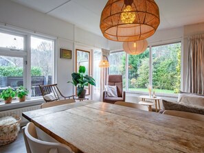 A dining area with a wooden table, chairs, and a hanging light fixture. - Boshuisje Juniper (De Koog)