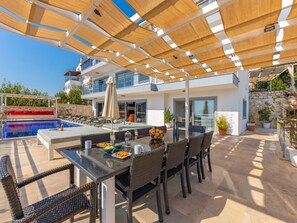 Ein Poolbereich mit Tisch und Stühlen, einem Schwimmbecken und einer überdachten Terrasse mit Pflanzen.