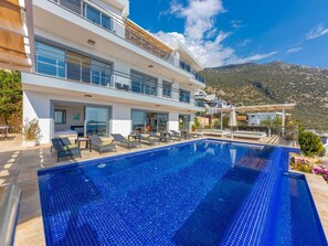 Ein modernes Hotel mit einem Dachpool im Infinity-Stil, Sitzgelegenheiten im Freien und Blick auf die Berge.