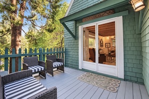 A green building with a sign reading 'GREEN GABLES' and a covered outdoor seating area with wicker furniture. - Classic Mountain Cottage | Near Lake & SkyPark + Trails | Green Gables Cottage (Lake Arrowhead)