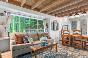 A cozy living room with a sofa, coffee table, and wooden dining table. - Classic Mountain Cottage | Near Lake & SkyPark + Trails | Green Gables Cottage (Lake Arrowhead)