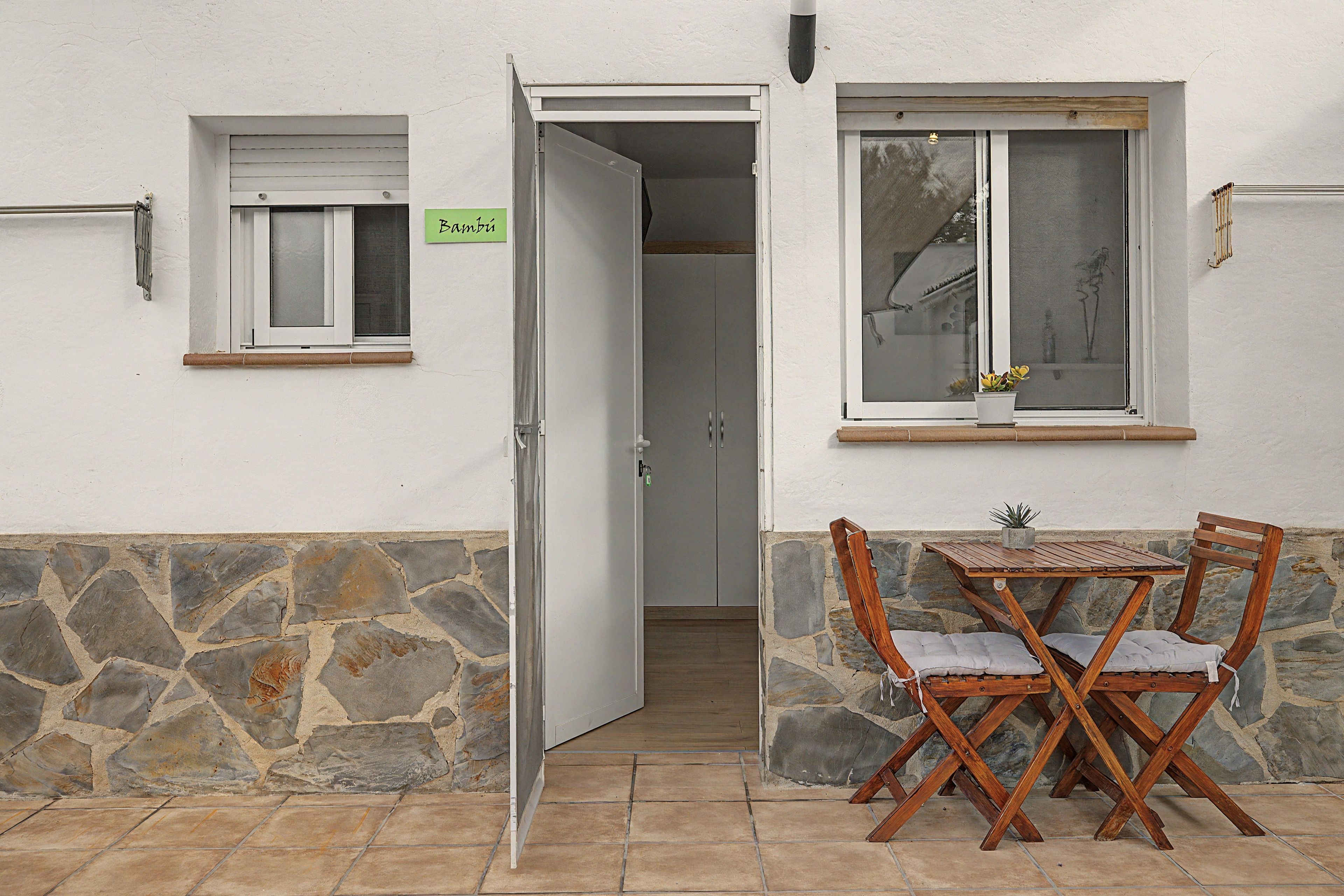 Une pièce avec un mur en pierre, une table en bois avec des chaises, une fenêtre donnant sur un paysage agréable et une porte menant à une autre pièce.