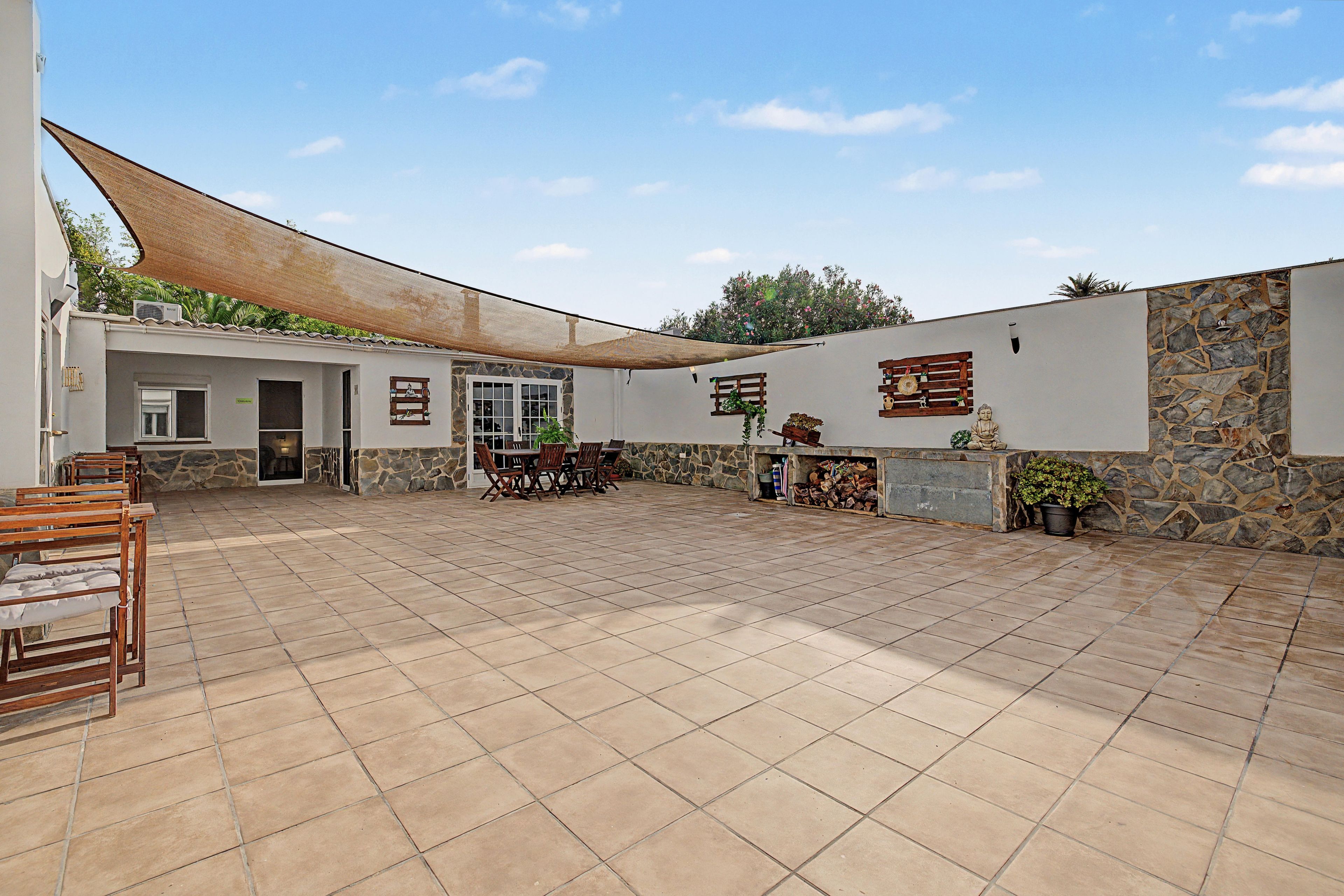 Un patio cubierto con pared de piedra, una mesa de madera con sillas y una estatua de Buda.
