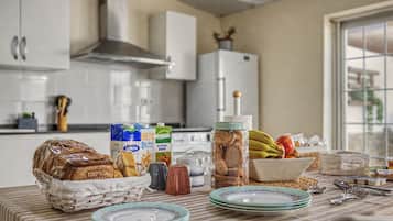 Una cocina con una mesa dispuesta para una comida, incluyendo pan, leche y un bol de fruta.