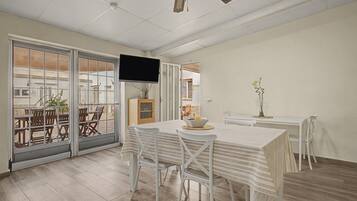 A dining area with a table and chairs, a television mounted on the wall, and a view through a glass door to an outdoor patio.
