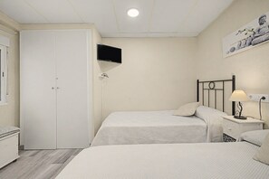 Een slaapkamer met twee bedden, een aan de muur bevestigde televisie, een nachtkastje met een lamp en een garderobe.