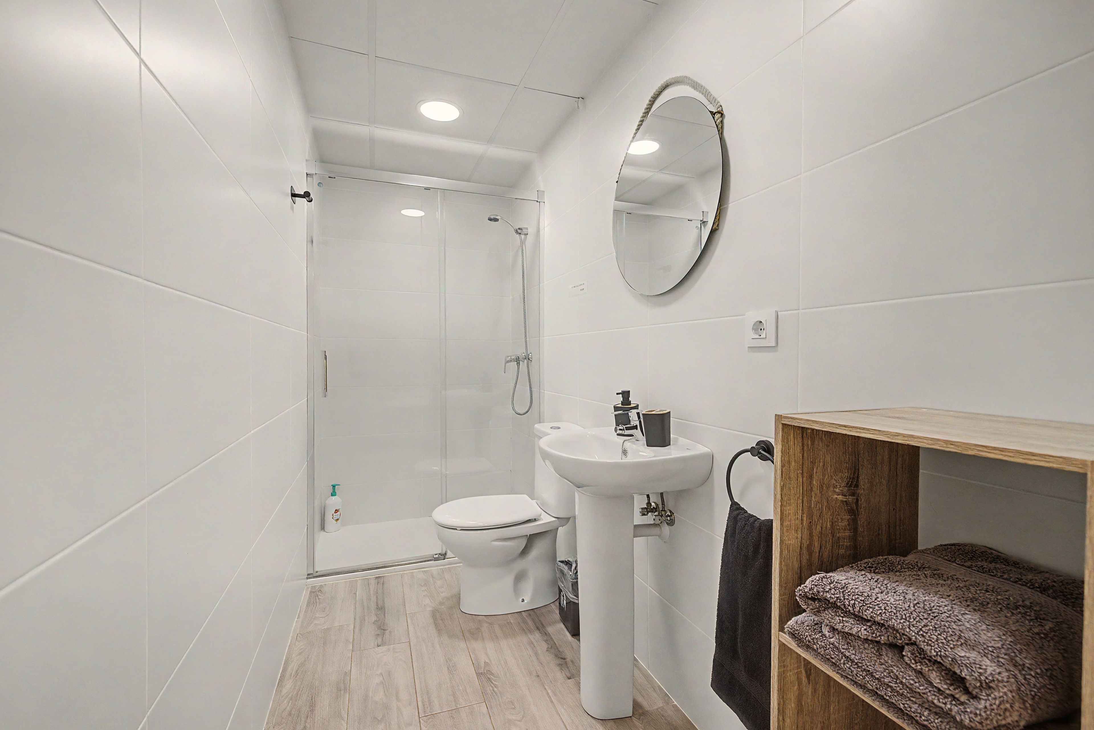 Une salle de bain moderne équipée d’une douche, de toilettes, d’un lavabo et d’une étagère en bois où sont rangées des serviettes.
