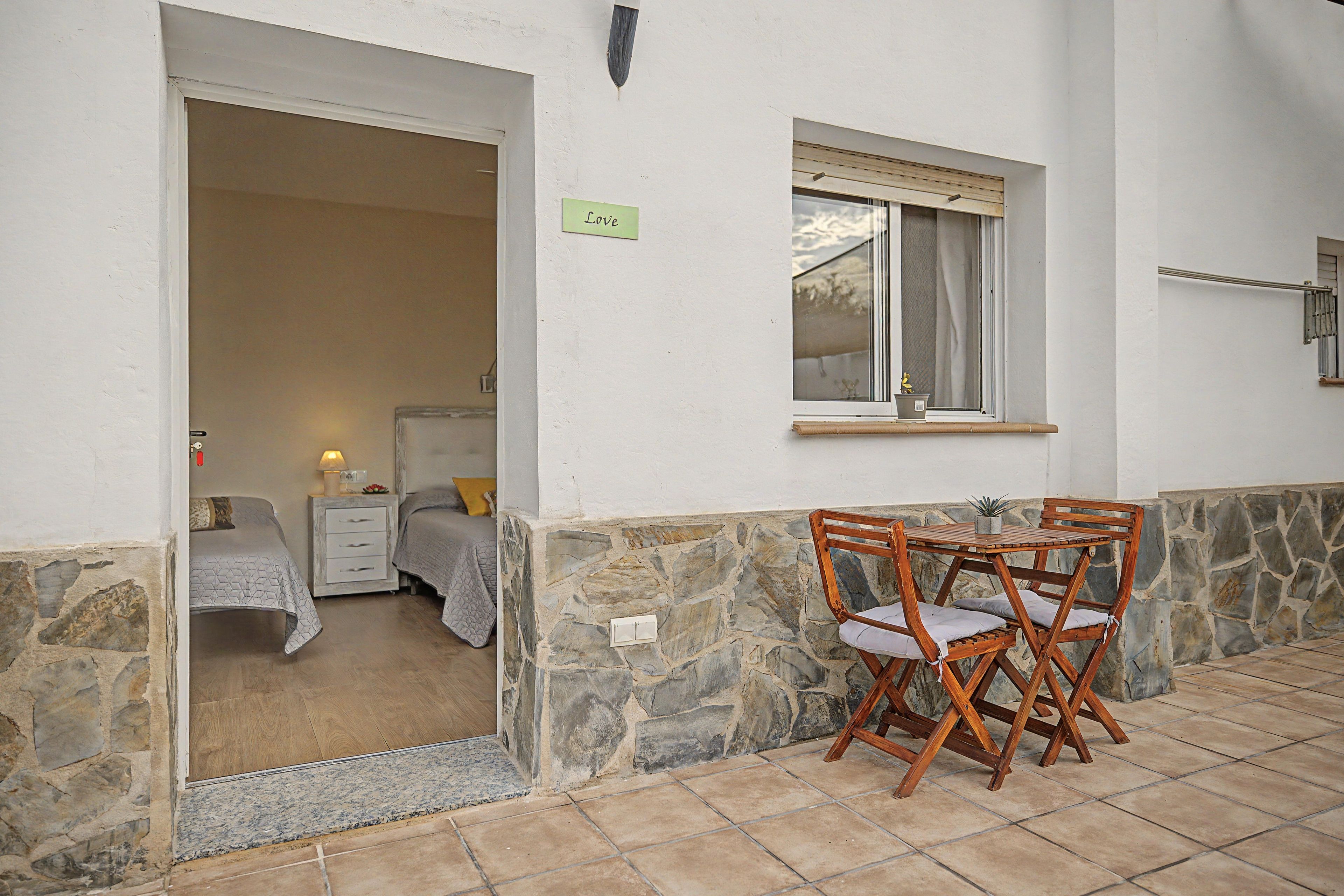 Una habitación con cama, mesita de noche, una pequeña mesa con lámpara y ventana con vistas.