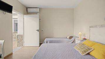 Een slaapkamer met twee bedden, een witte deur, een klein nachtkastje met een lamp en een aan de muur bevestigde airconditioner.