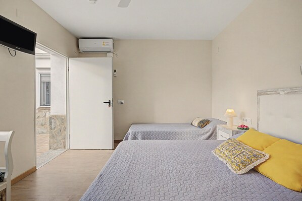 Une chambre avec deux lits, une porte blanche, une petite table de chevet avec une lampe et un climatiseur fixé au mur.