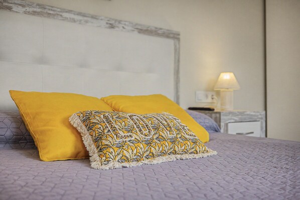 A bed with two pillows, one plain and one with a leaf pattern, and a nightstand with a lamp.