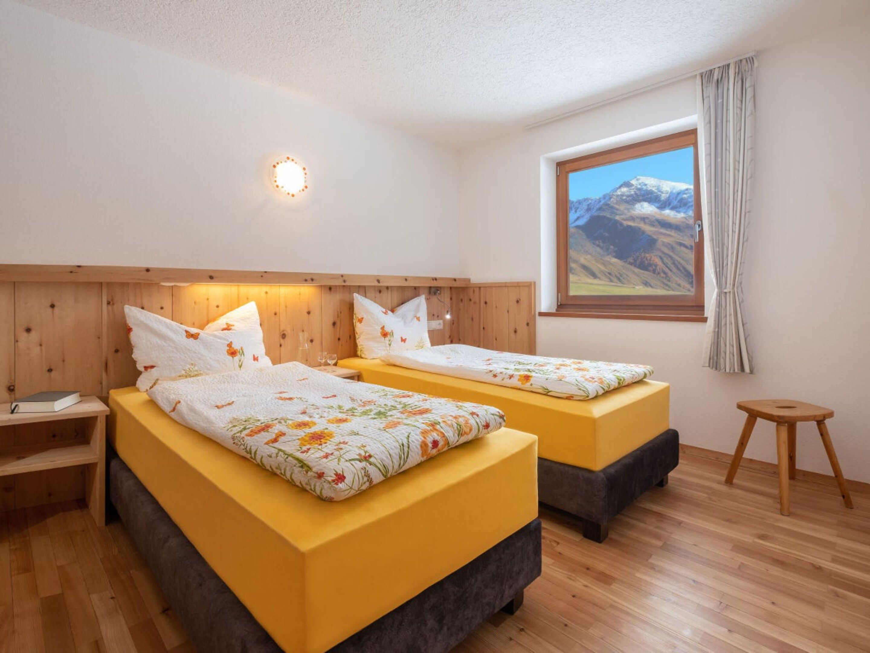 A hotel room with two beds, wooden headboard, a window with a mountain view, and a small stool.