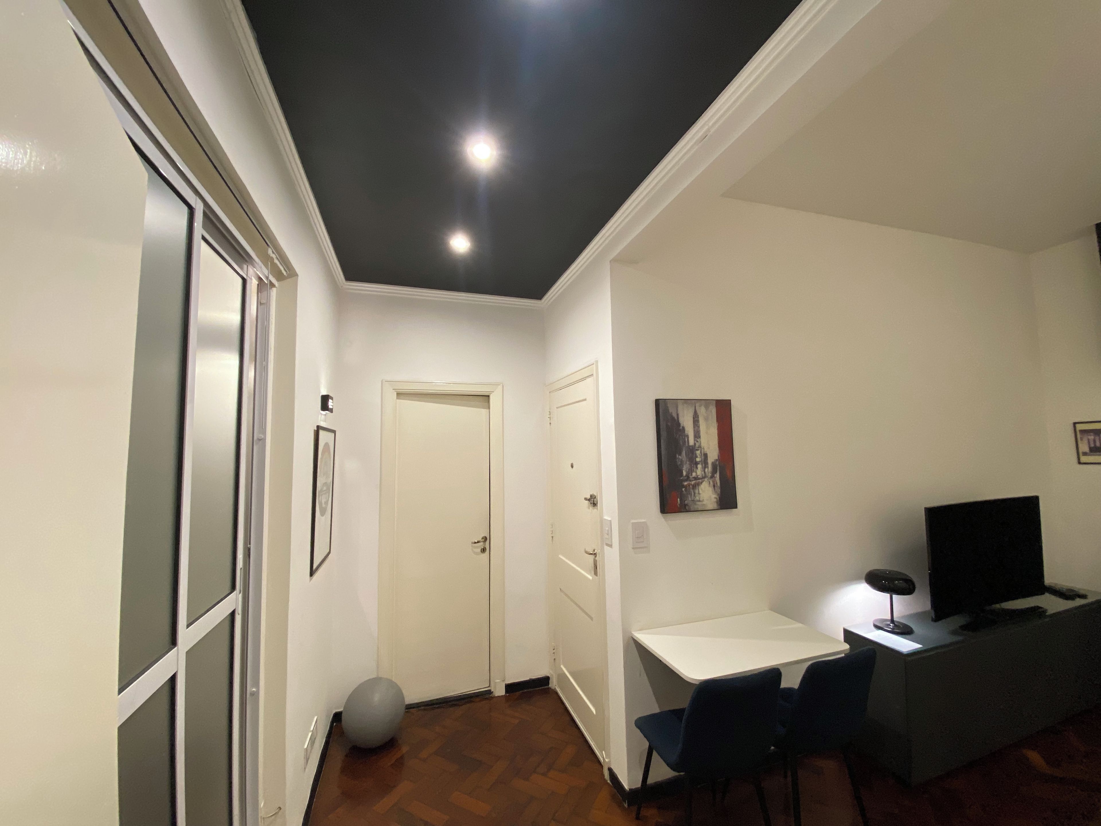 A room with a white desk, a chair, a television, and a painting on the wall.