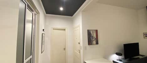 A room with a white desk, a chair, a television, and a painting on the wall.