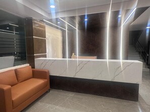 A reception area with a marble counter, a sofa, and a staircase in the background. - The Wise Hotel (Hyderabad)