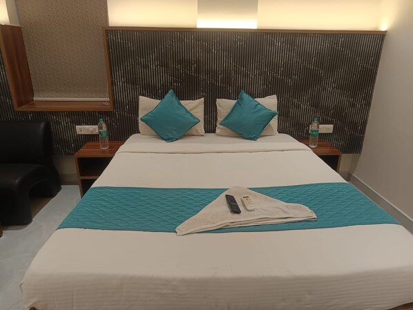 Habitación de hotel con una cama, dos mesitas de noche, un control remoto y una botella de agua.