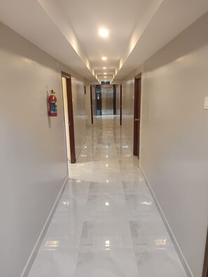 Un pasillo de hotel con un extintor de incendios montado en la pared, puertas a ambos lados y un piso de baldosas brillantes.