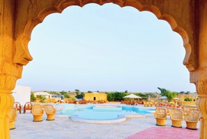 A courtyard with a pool, wicker chairs, and a building in the background.