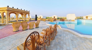 Un espace aménagé au bord de la piscine, avec des fauteuils en osier et un kiosque.