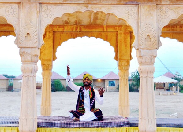 A person seated on a checkered mat under a decorative archway.