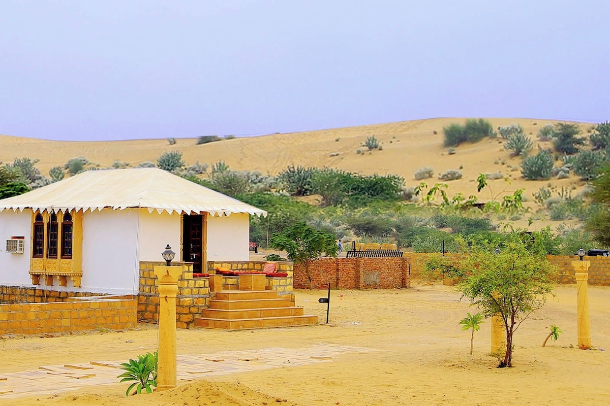A desert landscape with a small white building featuring a tiled entrance and a covered porch.