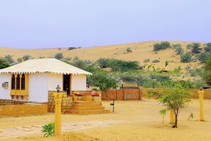 A desert landscape with a small white building featuring a tiled entrance and a covered porch.