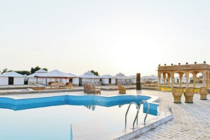 Una piscina con una fuente de agua cristalina azul, rodeada de tiendas de estilo tradicional y un pabellón con asientos.