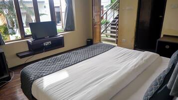 Un dormitorio con una cama, un televisor sobre un mueble bajo, una ventana con cortinas y vistas a una escalera exterior.