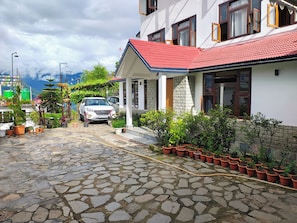 A paved driveway leading to a house with a red roof, surrounded by potted plants and a parked car. - Rumtek Heritage Resort (Rumtek)