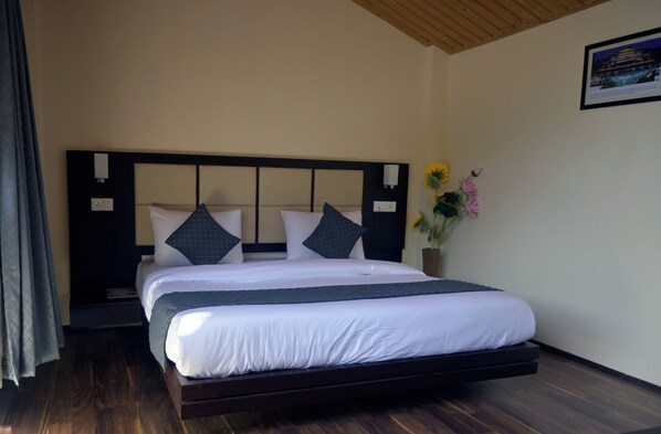 A hotel room with a bed, a nightstand, a vase with flowers, and a framed picture on the wall.