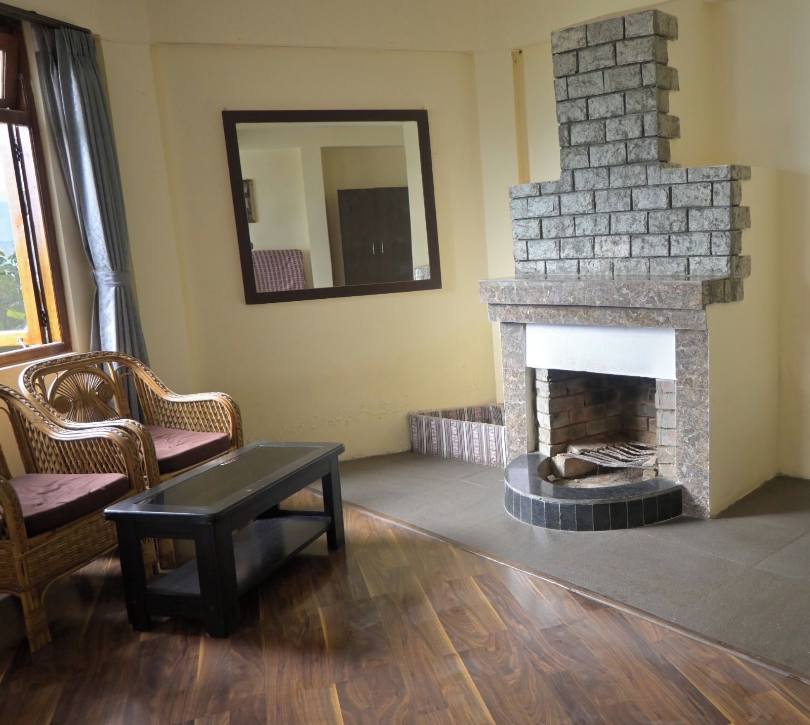 Una sala de estar con chimenea de piedra, muebles de mimbre y un espejo grande en la pared.