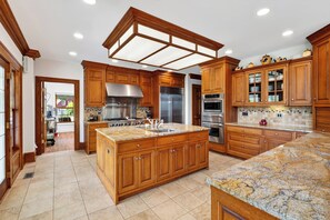 A spacious kitchen with wooden cabinets, a large island, stainless steel appliances, and a tiled backsplash. - Private Lake + Pool + Tennis | Dock, Canoes + Fire Pit | The Lake Ellis Lodge (Wingdale)