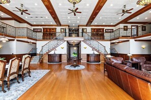 A spacious interior with a grand staircase, wooden flooring, and a seating area with leather sofas. - Private Lake + Pool + Tennis | Dock, Canoes + Fire Pit | The Lake Ellis Lodge (Wingdale)