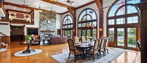 A spacious interior with a high ceiling, wooden beams, a stone fireplace, and large arched windows.