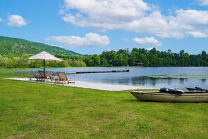 A lakeside setting with a dock, lounge chairs, and a boat. - Private Lake + Pool + Tennis | Dock, Canoes + Fire Pit | The Lake Ellis Lodge (Wingdale)
