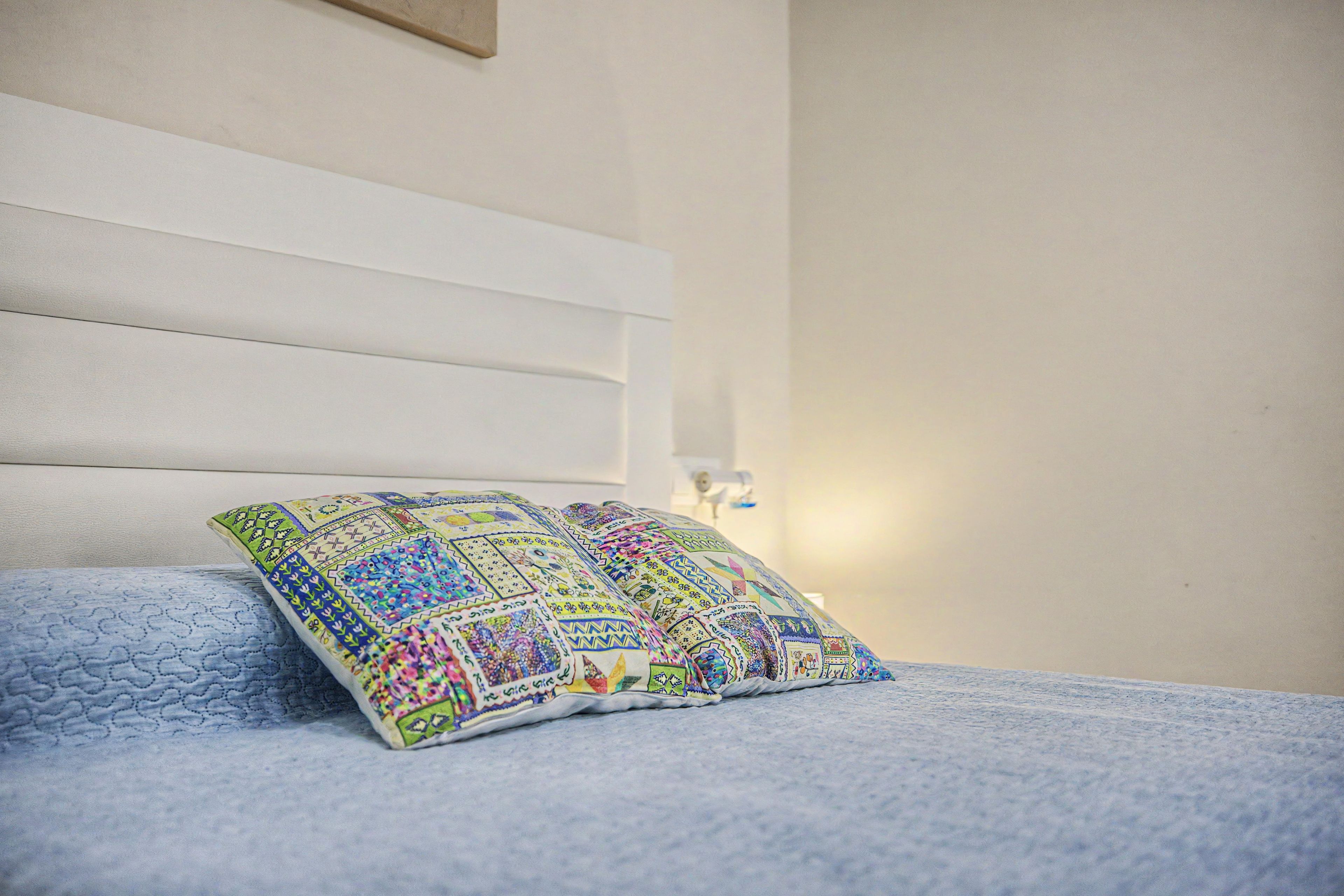 A bed with a blue quilt and a colorful pillow with a geometric pattern.