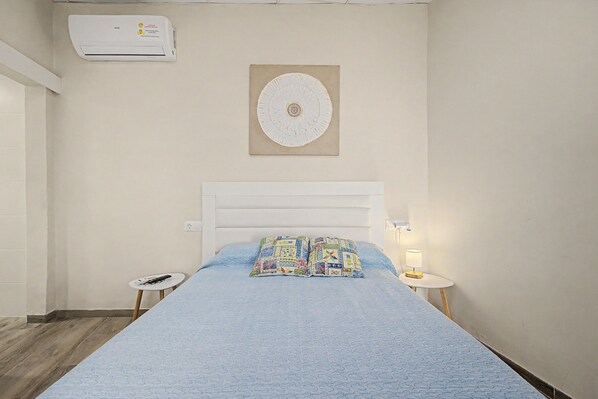 A bedroom with a bed, a wall-mounted air conditioner, a decorative plate, a bedside table with a lamp, and a remote control on a small table. - Room 'Namaste' with shared terrace, Wi-Fi and air conditioning (Poblenou del Delta)