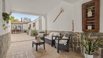Un patio techado con mobiliario de mimbre, paredes de piedra y plantas en macetas.