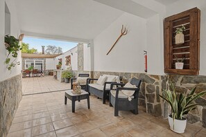 Ein überdachter Patio-Bereich mit Korbmöbeln, Steinmauern und Topfpflanzen.