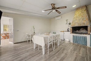 A dining area with a table and chairs, a ceiling fan, and a stone fireplace. - Room 'Namaste' with shared terrace, Wi-Fi and air conditioning (Poblenou del Delta)