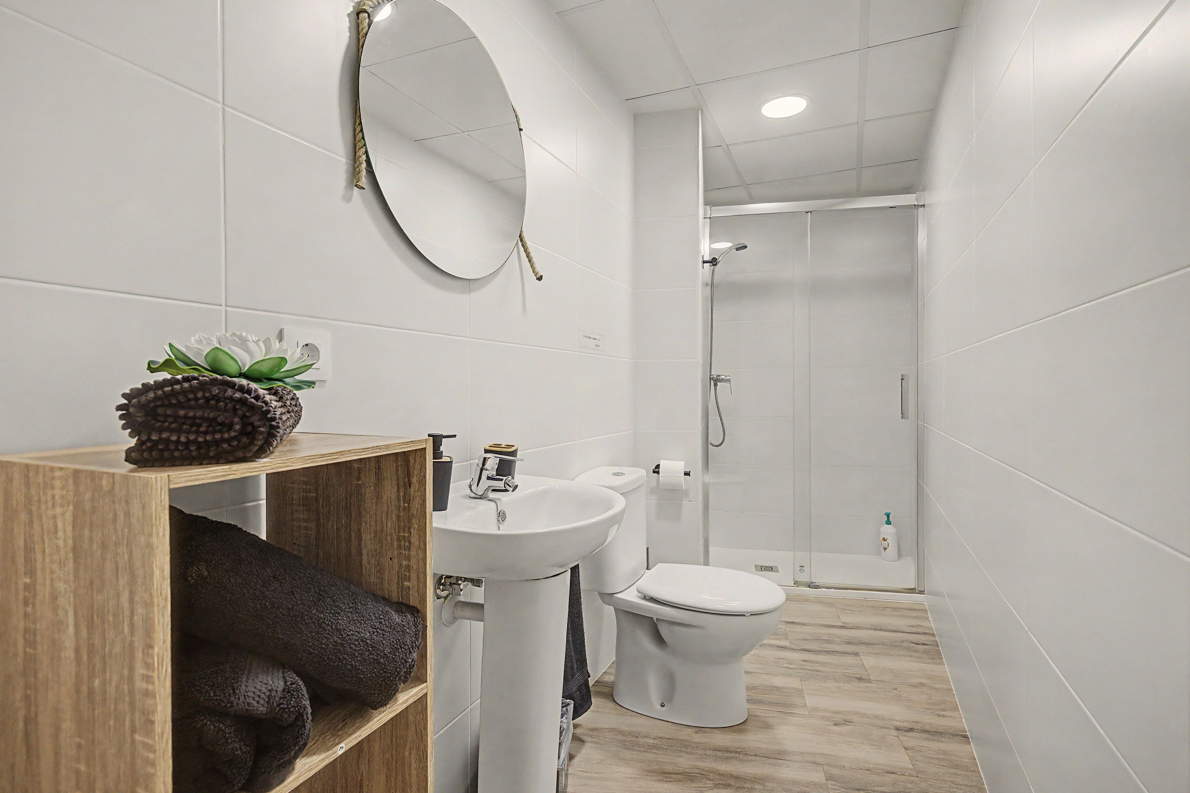 Un baño moderno con tocador de madera, lavamanos, inodoro y ducha.