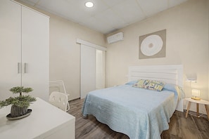 A bedroom with a bed, bedside table, lamp, and a potted plant.