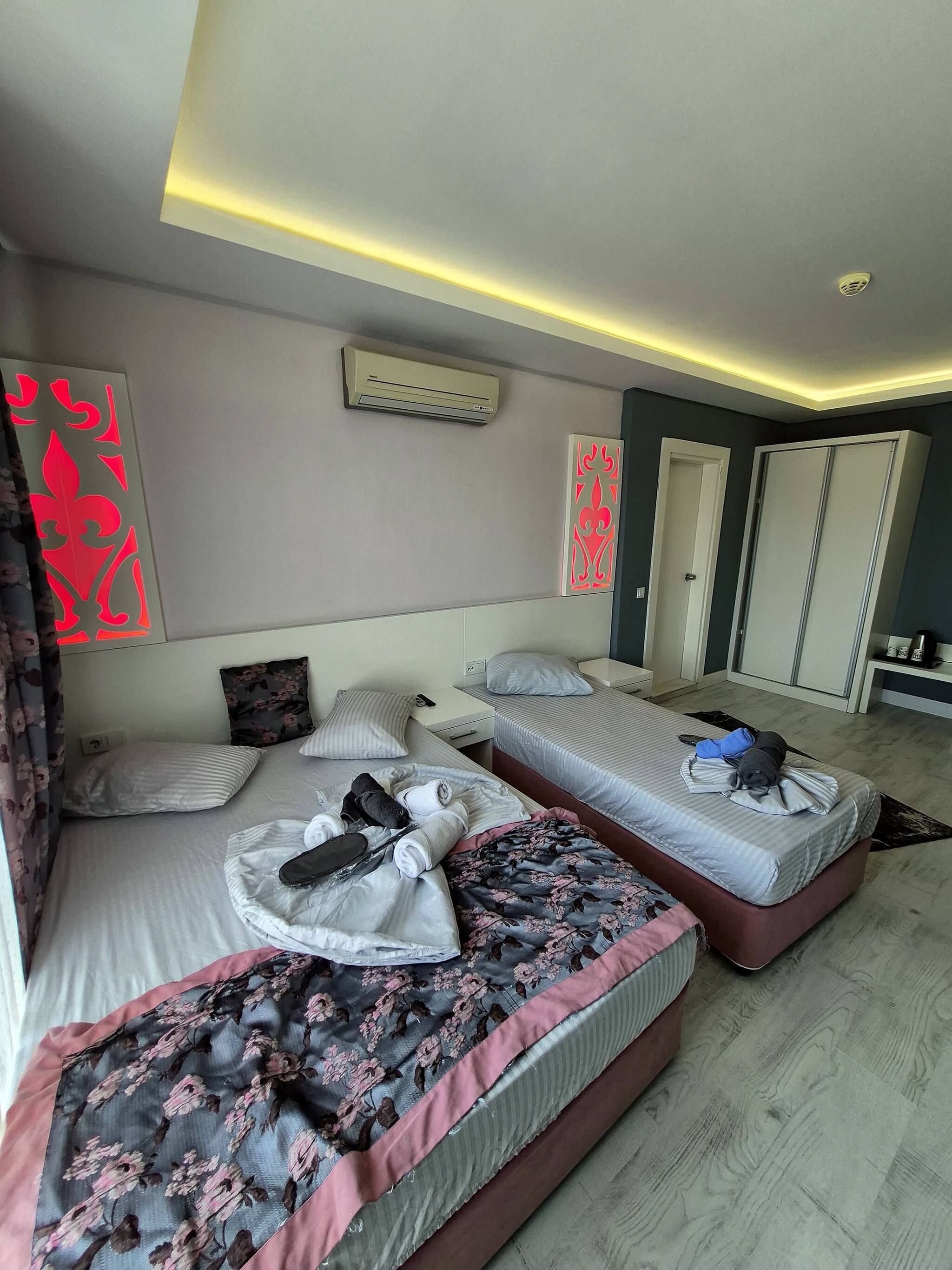 A hotel room with two beds, a wardrobe, an air conditioning unit, and a decorative wall panel.