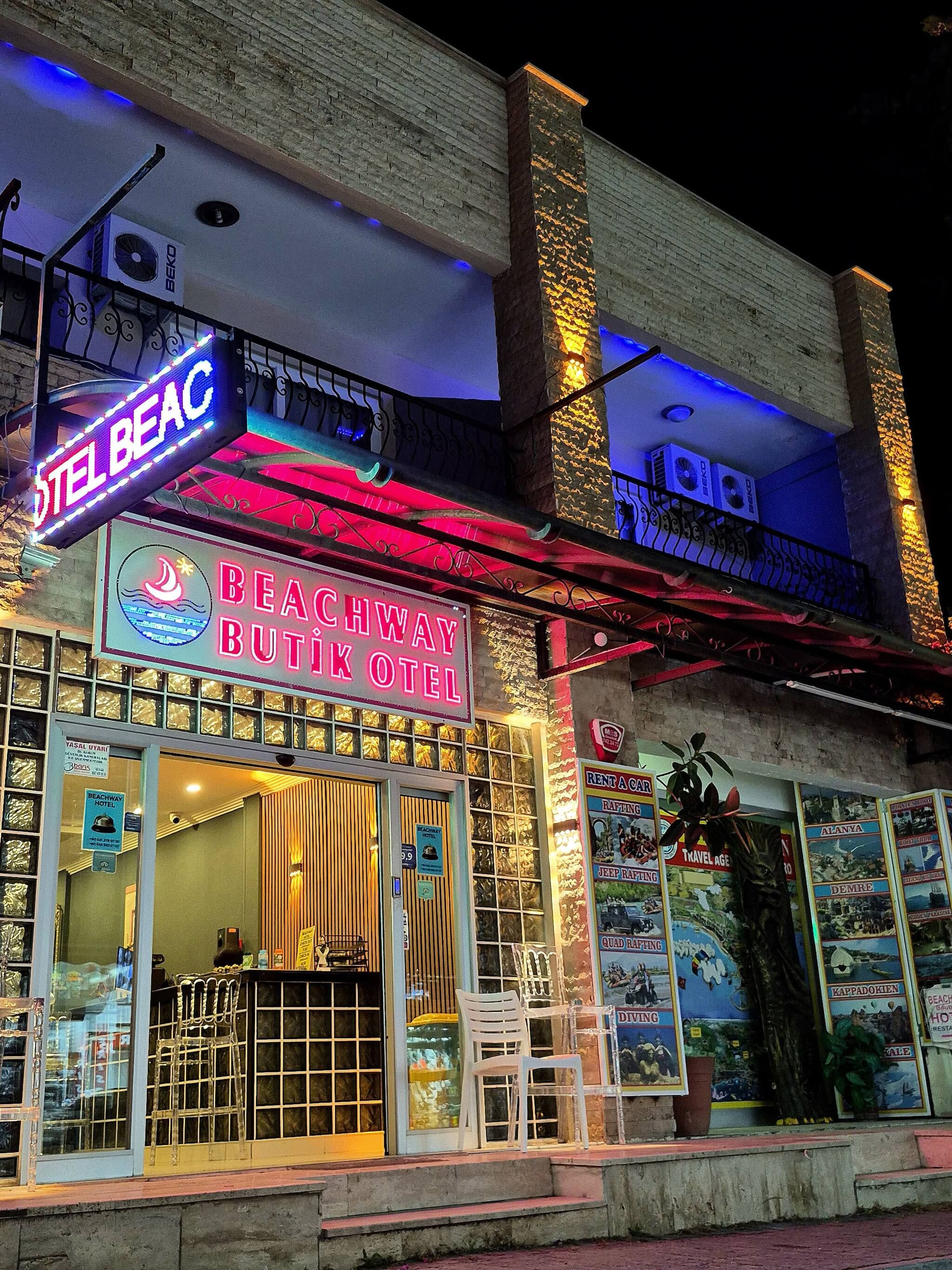 A hotel with a sign reading 'BEACHWAY BUTIK HOTEL' and a neon sign above it.